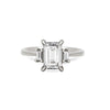 Thumbnail of Front view of the Hero Emerald Cut Three Stone Diamond Engagement Ring in 14k solid white gold, featuring a central 2ct emerald-cut diamond flanked by two smaller diamonds on a polished band.