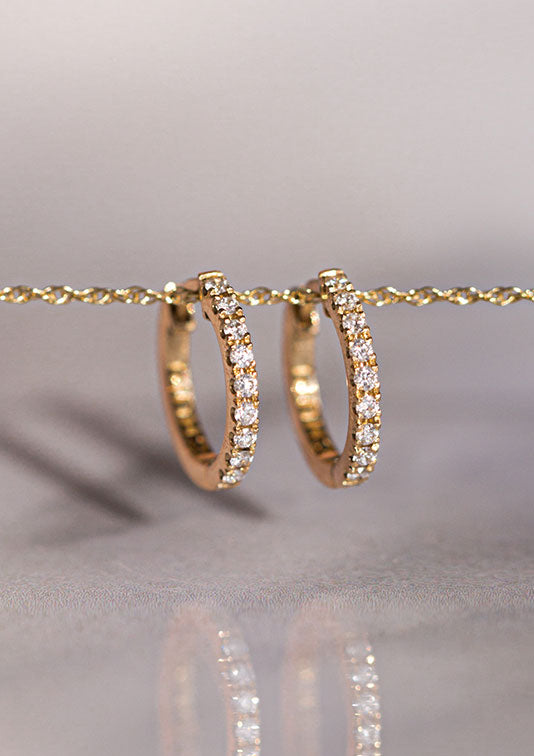 Two Eternity Huggie earrings suspended on a gold chain.